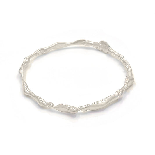 The Hoop Bangle by FR | Art Jewellery is shown with an organic, twisted design. Featuring an uneven, textured surface, it exudes a natural and unique charm. This piece of handmade jewellery is displayed against a white background and is available for custom-made orders.