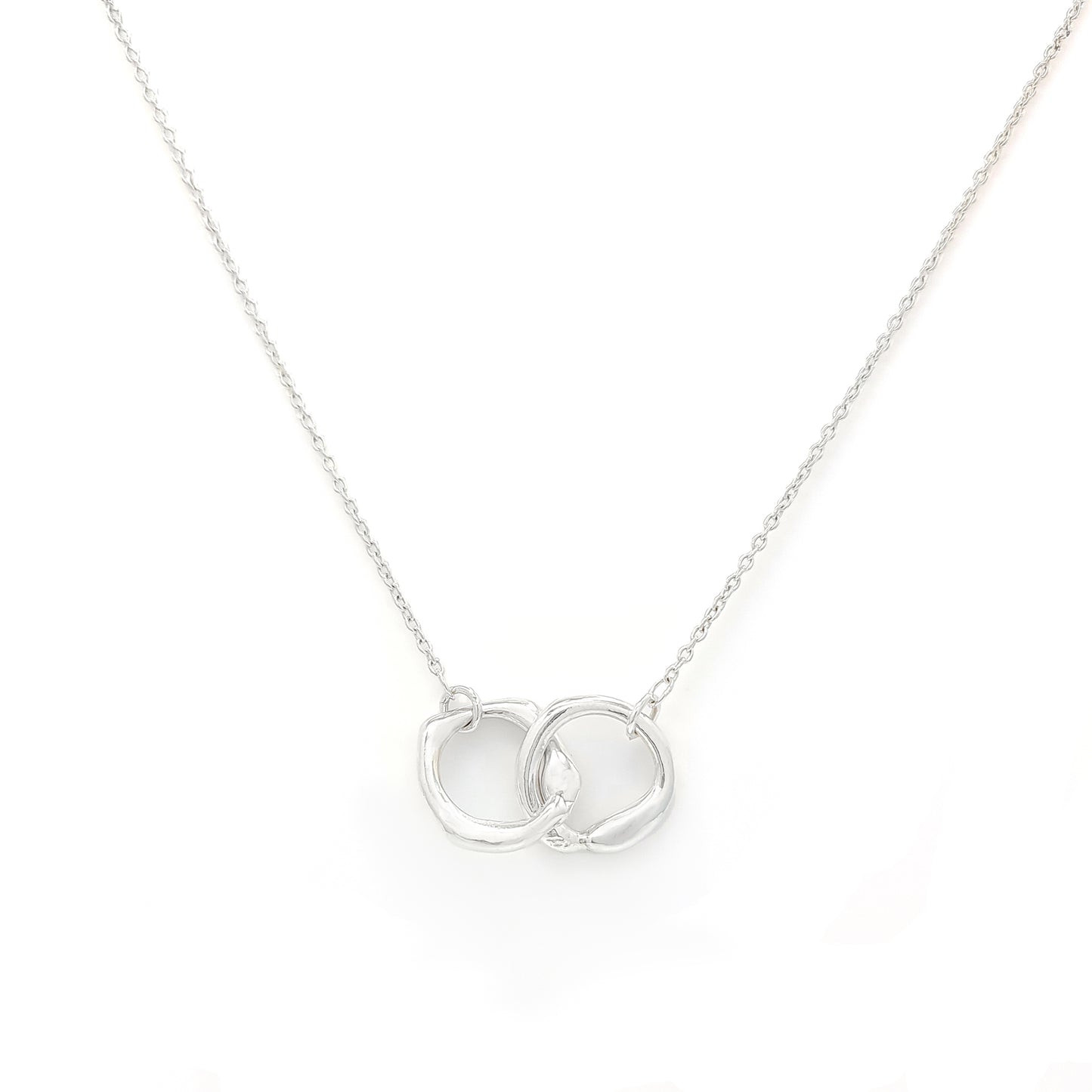 The Hoop Necklace by FR | Art Jewellery is a silver piece with a delicate chain that features two interlocking circular pendants. The pendants have a slightly irregular, textured appearance, creating a modern yet organic look. This handmade jewellery piece is laid flat against a plain white background.