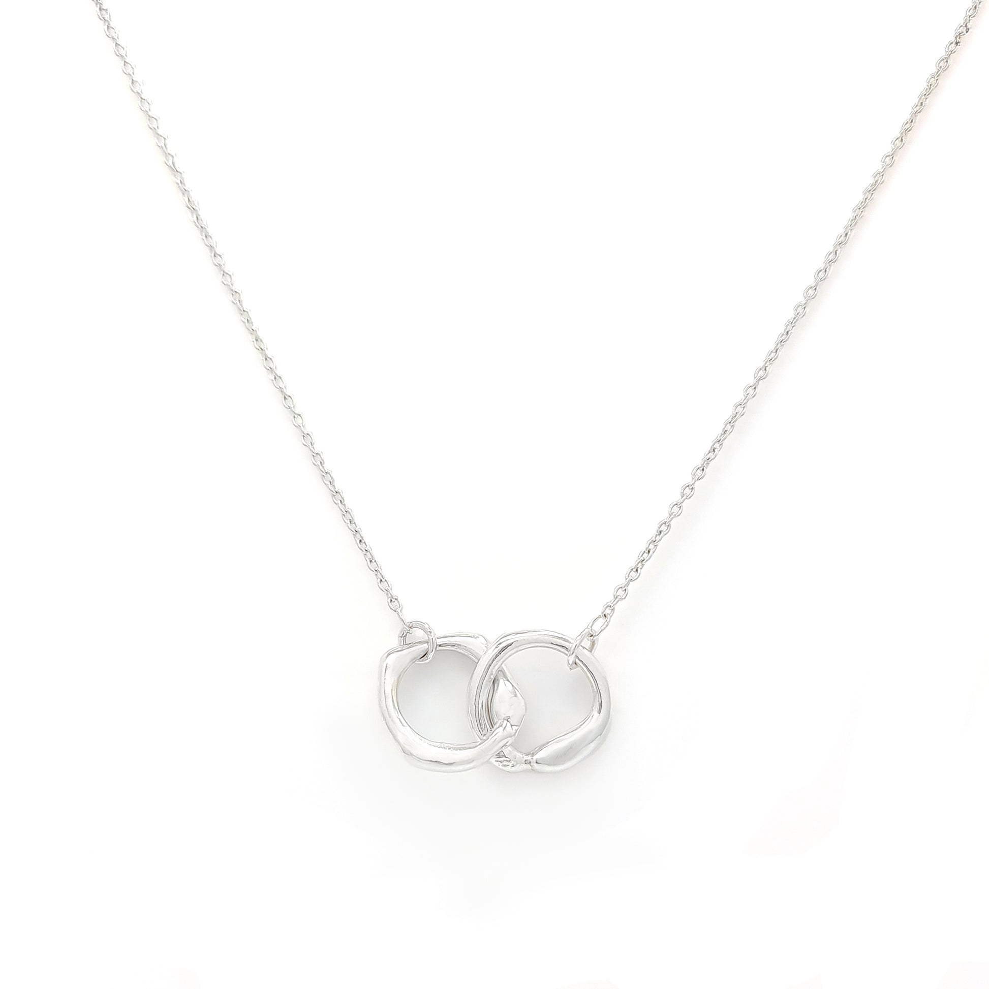 The Hoop Necklace by FR | Art Jewellery is a silver piece with a delicate chain that features two interlocking circular pendants. The pendants have a slightly irregular, textured appearance, creating a modern yet organic look. This handmade jewellery piece is laid flat against a plain white background.