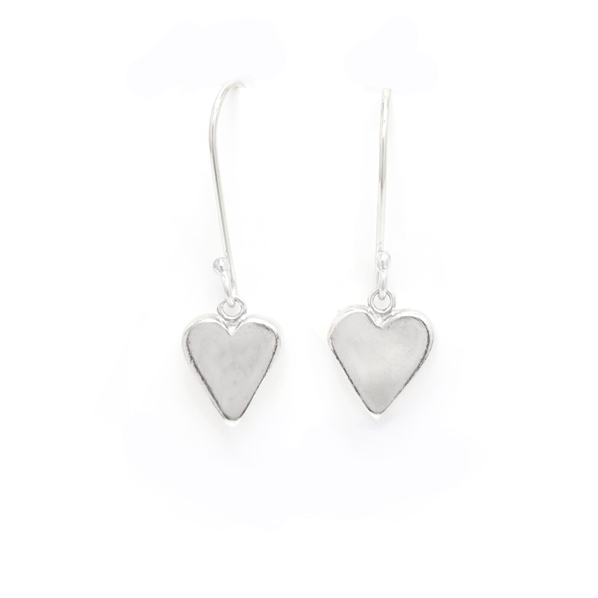 Introducing the "In Love Earrings" by FR | Art Jewellery, these handmade silver heart-shaped dangle earrings feature a smooth, polished surface that subtly reflects light. They hang gracefully from thin hooks and are showcased against a plain white background.