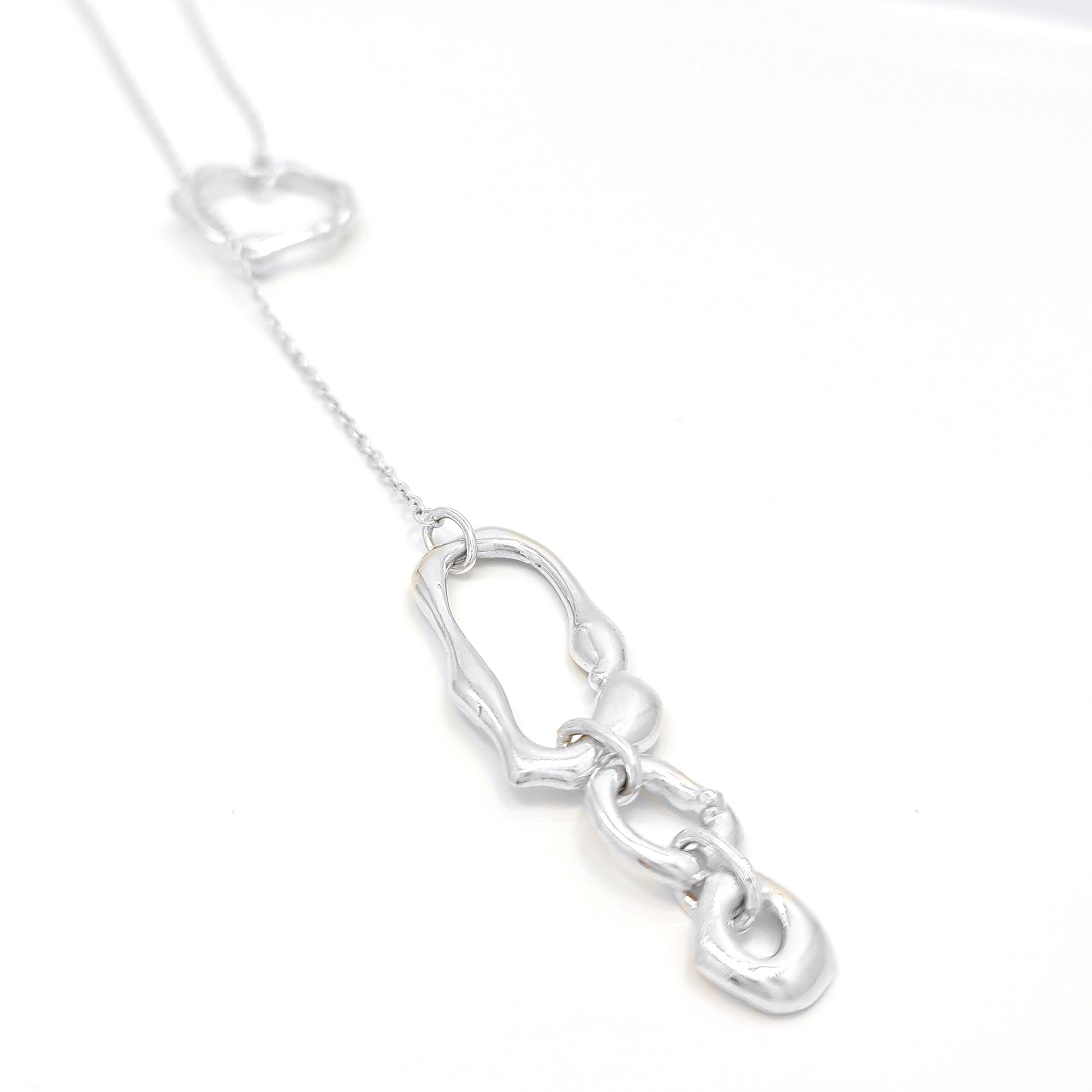 The Join Together Necklace by FR | Art Jewellery showcases a delicate design featuring a circular pendant connected by a thin chain to an asymmetrical, abstract shape. This minimalistic and elegant piece displays the abstract shape hanging below the circular pendant, creating a modern, artistic look. Each handmade piece of this jewellery can be custom-made to order.