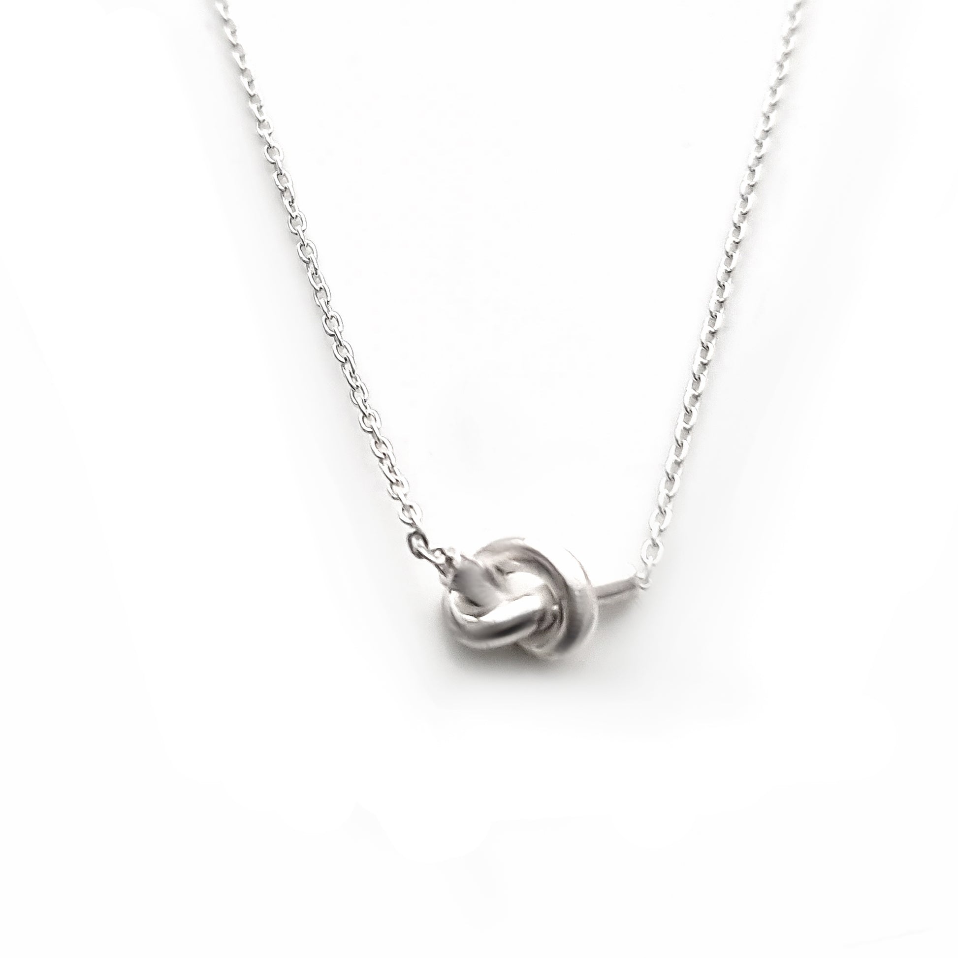 A delicate "Knot Necklace big chain small" by FR | Art Jewellery features a minimalist knot design at the center, set against a plain white background. This handmade jewellery piece showcases two intertwined loops, creating a simple yet elegant focal point.