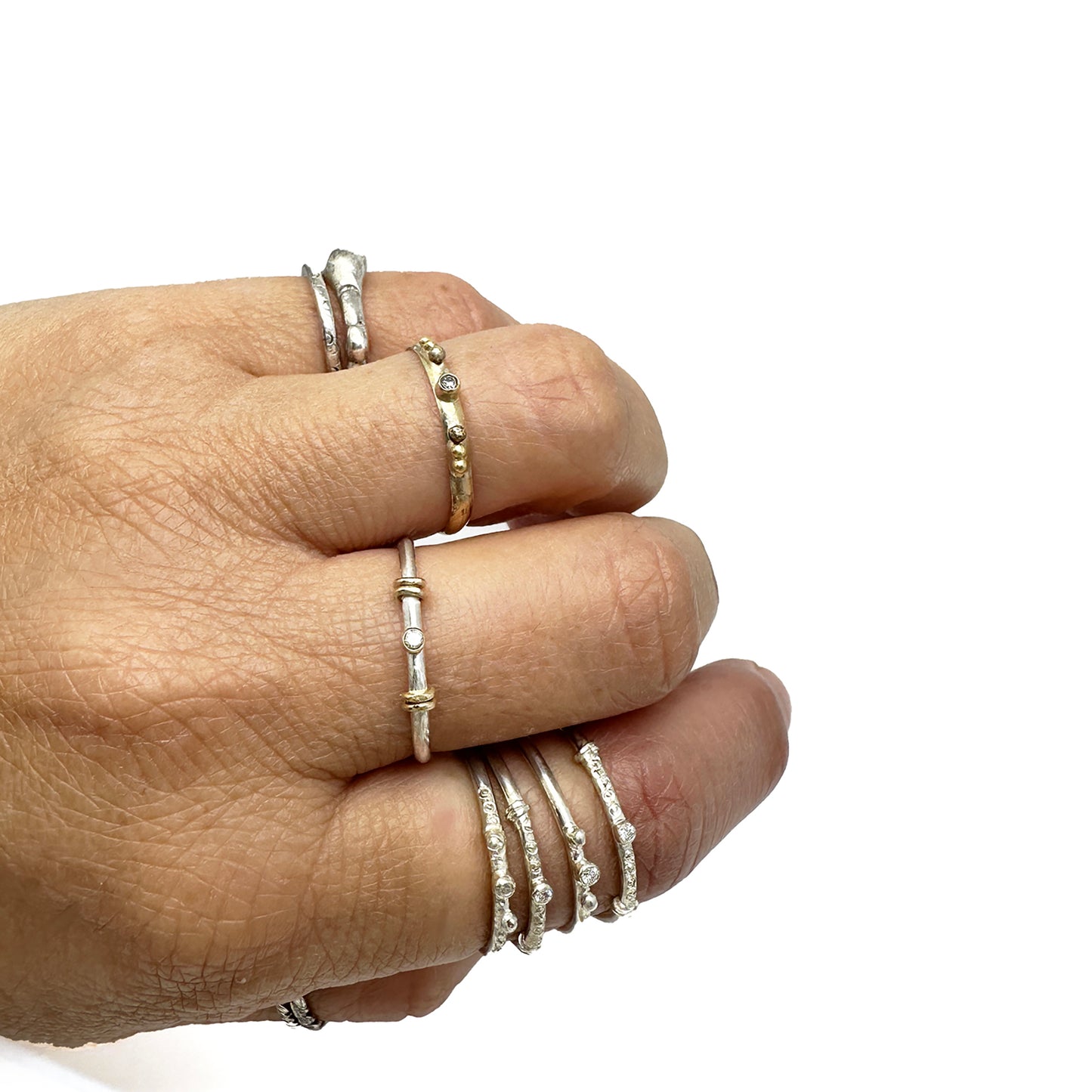 A collection of six Miniature Rings from FR | Art Jewellery is displayed on a white background. Five of the rings are crafted from silver with small gem accents, and one is gold, featuring a slightly larger central stone. Each handmade piece exhibits its own unique design and arrangement of stones.