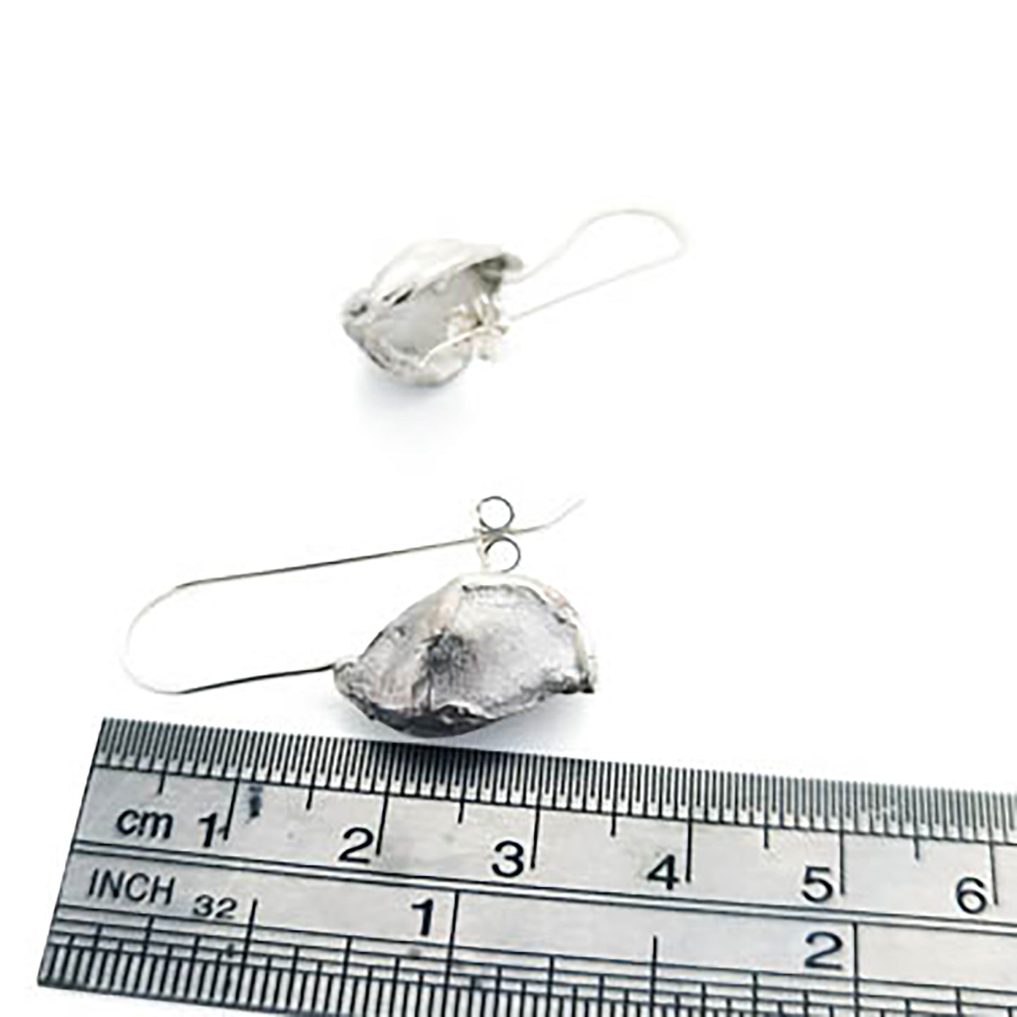 These Nut earrings from FR | Art Jewellery feature unique, organic shapes that resemble seeds or pods. As part of our handmade jewelry collection, each earring is attached to a simple wire hook for easy wearing. The shiny silver surface boasts a reflective finish with subtle textural details.