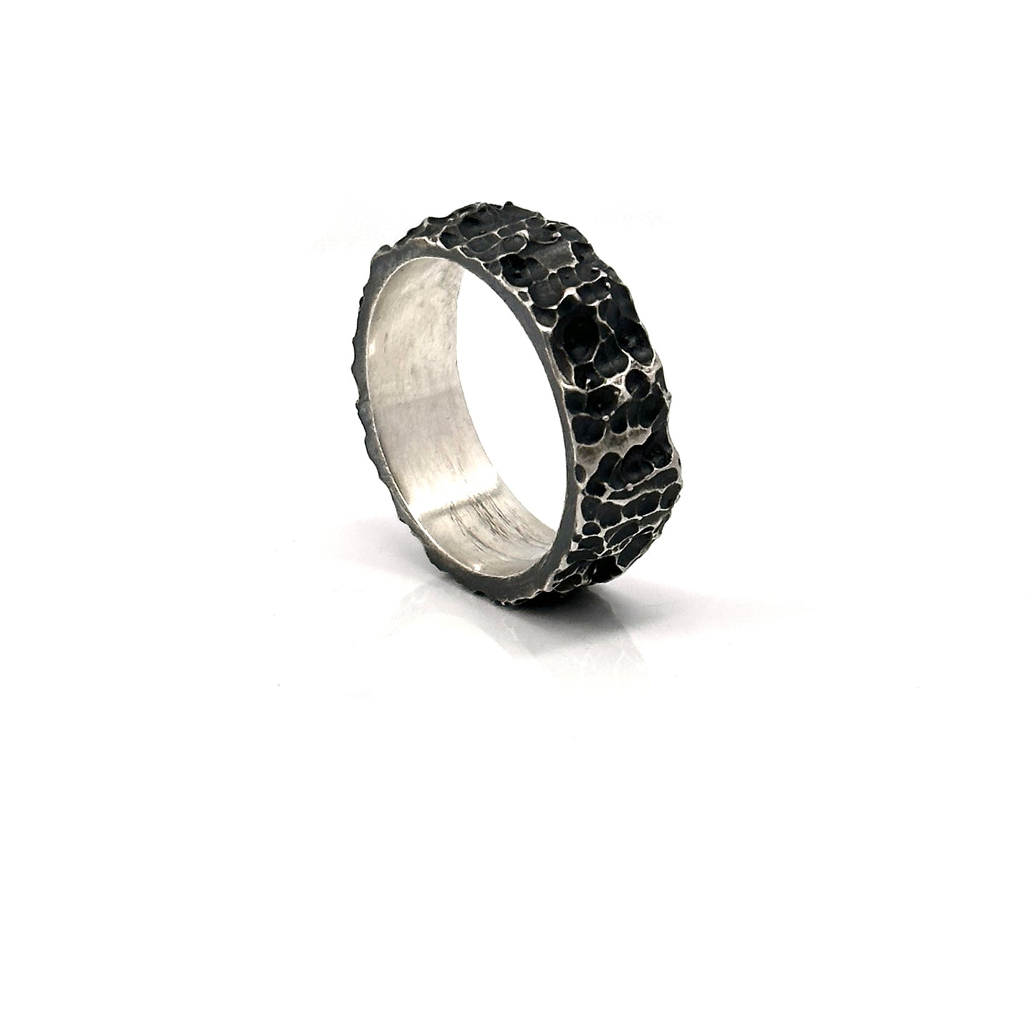 The Porocious Ring by FR | Art Jewellery features a rugged, textured silver surface reminiscent of natural rock formations. Its interior is smooth and polished, providing a striking contrast to the rough exterior. This piece of handmade jewellery is showcased upright against a plain white background.