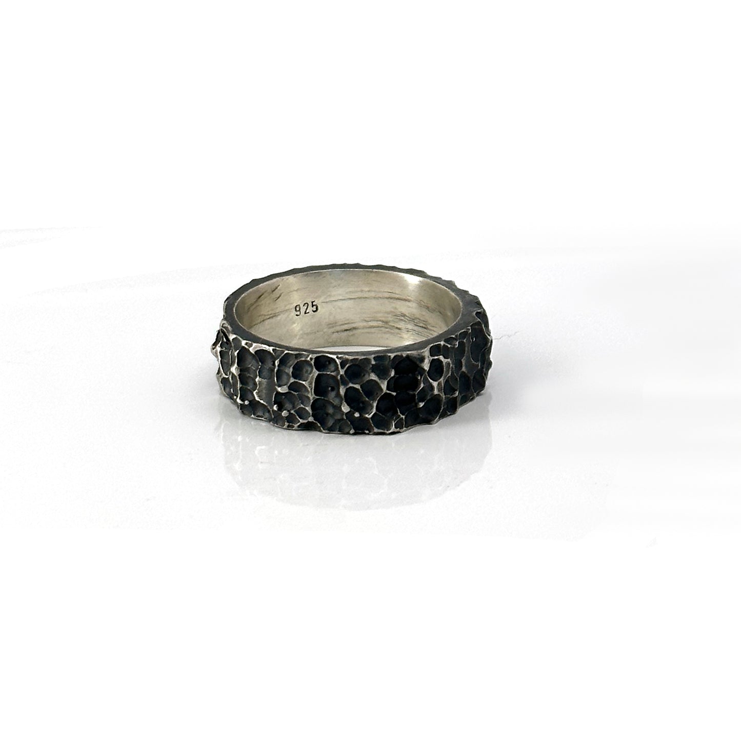 The Porocious Ring by FR | Art Jewellery features a rugged, textured silver surface reminiscent of natural rock formations. Its interior is smooth and polished, providing a striking contrast to the rough exterior. This piece of handmade jewellery is showcased upright against a plain white background.