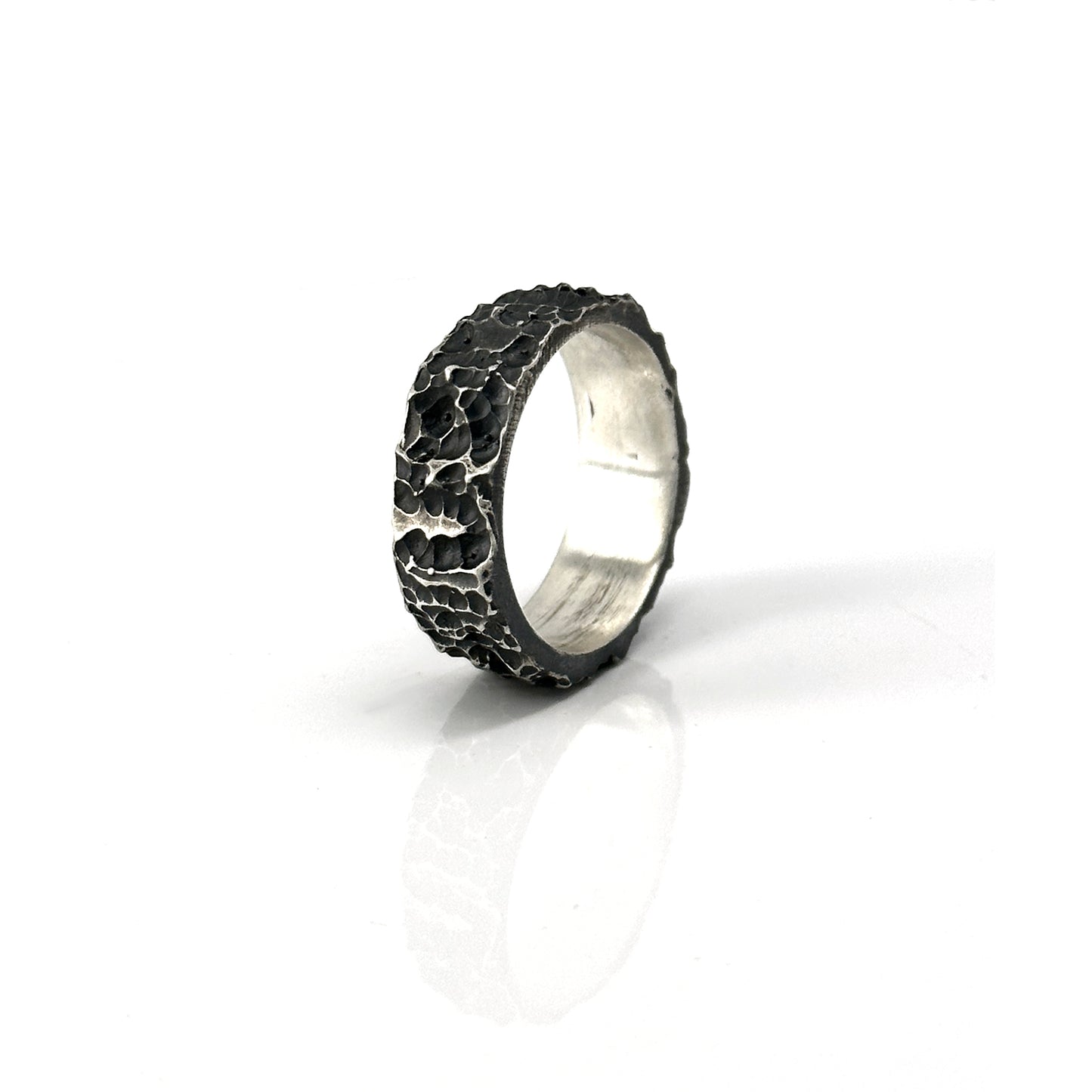 The Porocious Ring by FR | Art Jewellery features a rugged, textured silver surface reminiscent of natural rock formations. Its interior is smooth and polished, providing a striking contrast to the rough exterior. This piece of handmade jewellery is showcased upright against a plain white background.