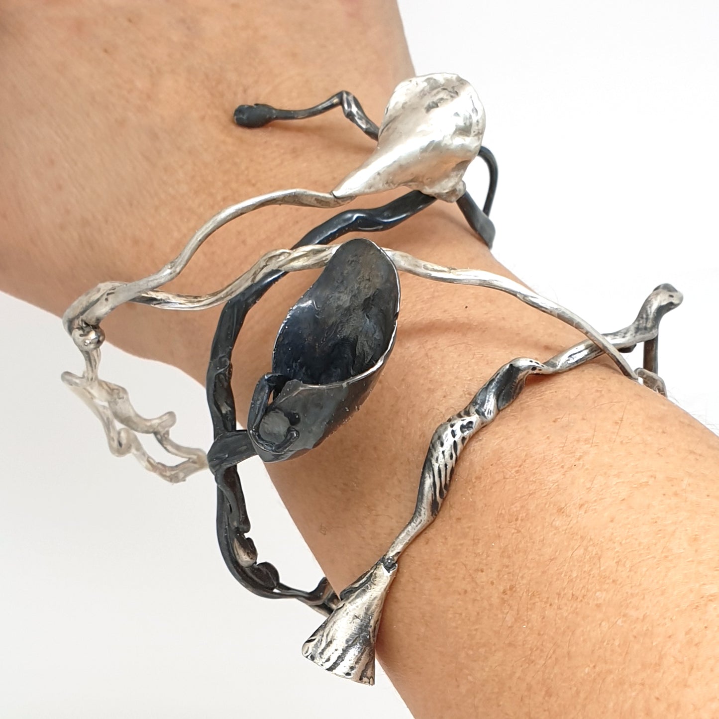 The Seaweed Bangle Sterling Silver by FR | Art Jewellery is an abstract metallic sculpture with twisting, irregular silver and black rods ending in organic, flower-like forms, displayed on a white background.