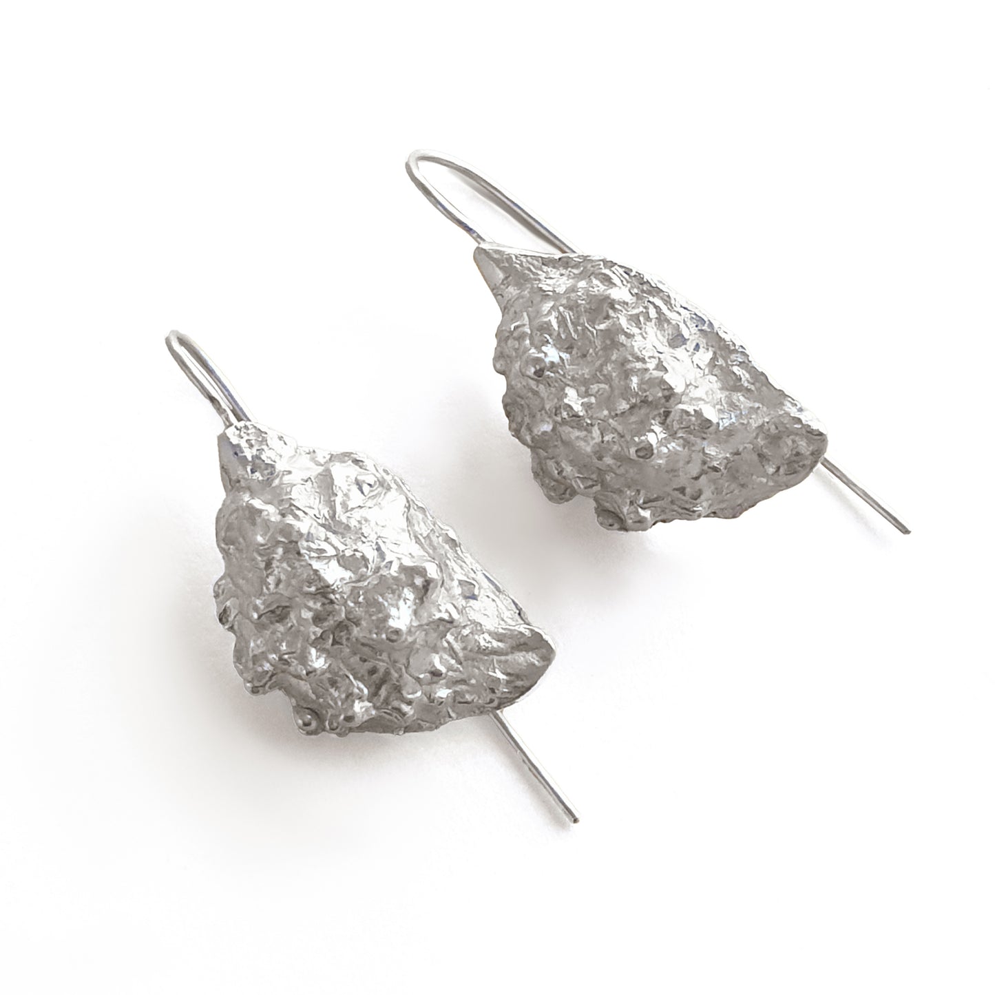 Introducing the Seeded earrings from FR | Art Jewellery: a stunning pair of silver earrings with an organic, textured design. Resembling small, rough mineral chunks, these unique pieces are attached to thin hooks for easy wearing. Ideal for enthusiasts of handmade jewellery, the metallic surface pops beautifully against any background.