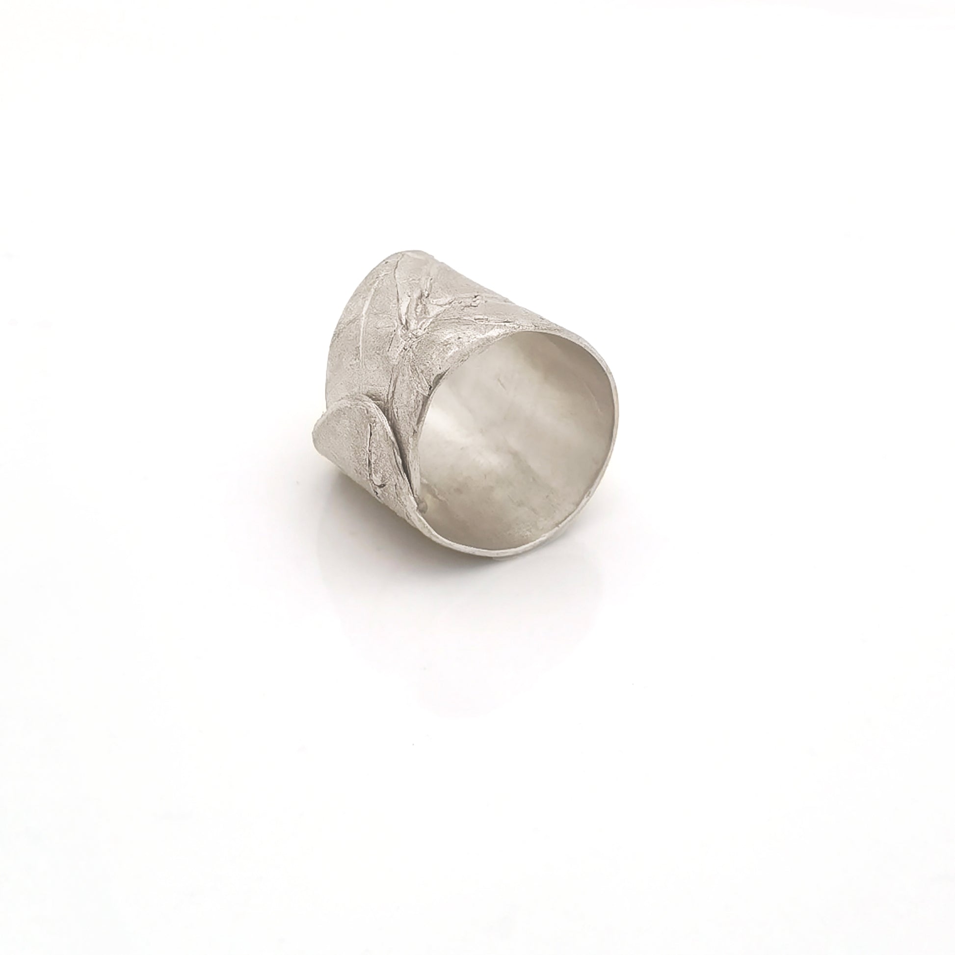 A wide, silver, adjustable "Silver Leaf Ring" by FR | Art Jewellery is placed on a plain white background. Part of the "Inspired by Nature Collection," the ring features subtle leaf patterns and has a textured, matte finish, giving it an organic and earthy appearance.