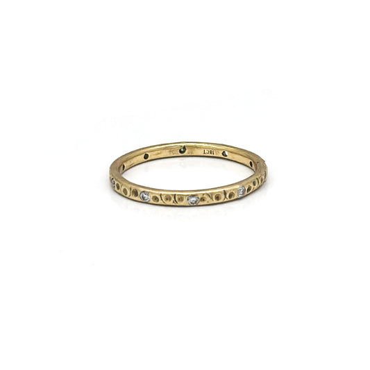 The Gloria Ring by FR | Art Jewellery is a delicate gold band adorned with small, evenly spaced diamonds. The ring features a subtle texture with tiny indentations and occasional darkened areas, giving it a vintage or antique appearance that evokes the charm of custom-made jewellery. It is beautifully set against a plain white background.