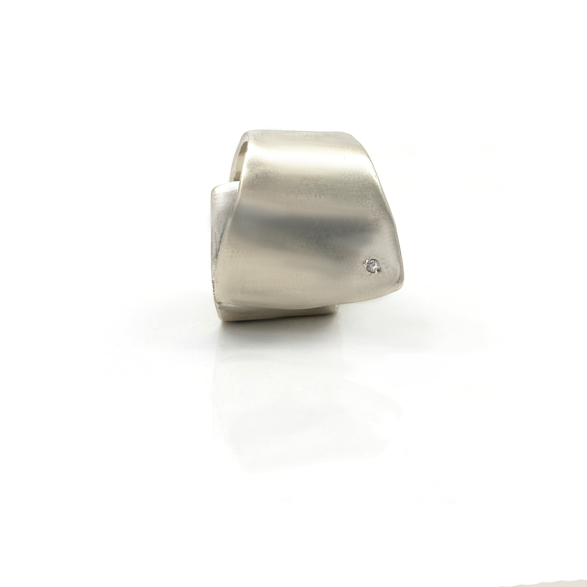 The Spiral Flow Ring by FR | Art Jewellery is a modern sterling silver ring featuring a smooth, sculptural form and a small inset diamond, shown on a white reflective surface.