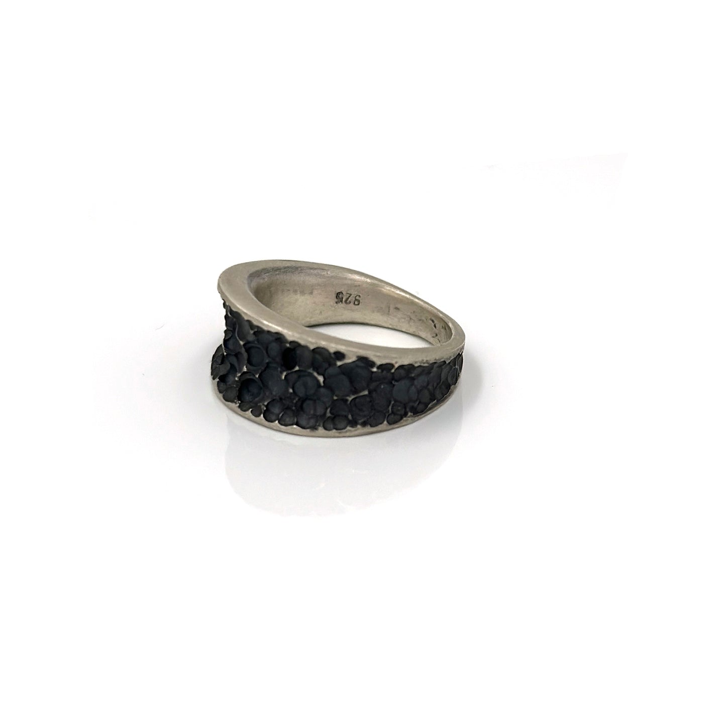 The Spot Ring by FR | Art Jewellery is a silver accessory with a wide band, showcasing a textured, hammered surface design. It boasts a shiny, polished finish and is displayed against a plain white background, exemplifying exquisite handmade jewellery craftsmanship.