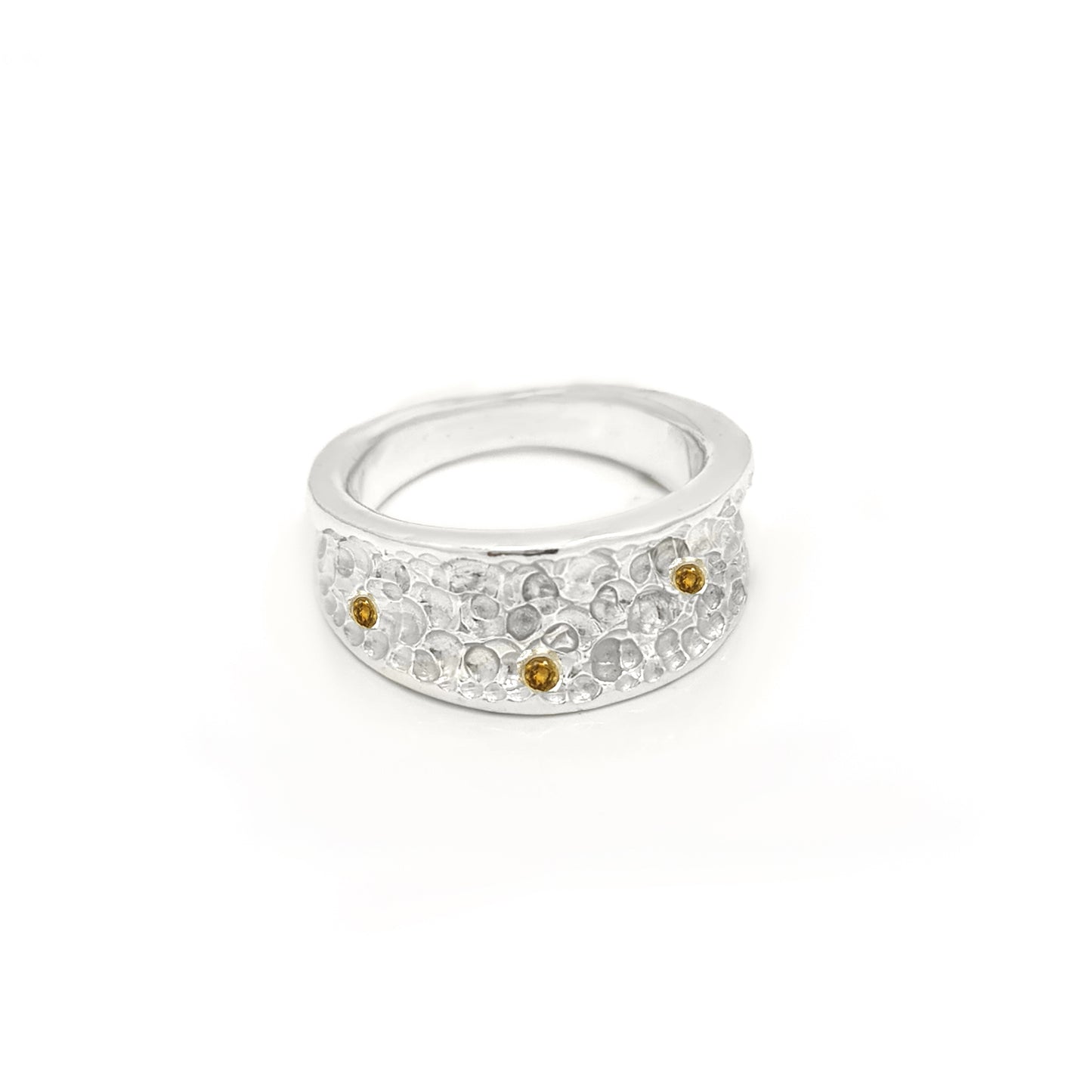 The Spot of Light Ring from FR | Art Jewellery boasts a wide silver band embellished with an intricate floral pattern. The design is accentuated by small, yellow gemstones that are evenly spaced, adding a touch of color and elegance. The white background highlights the handmade jewellery details of this exquisite piece.