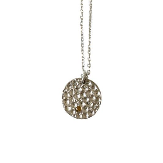 The Spot Of Light Big Sterling Silver Necklace by FR | Art Jewellery features a round, textured silver pendant with small raised bumps and a single citrine gemstone, shown on a plain white background.