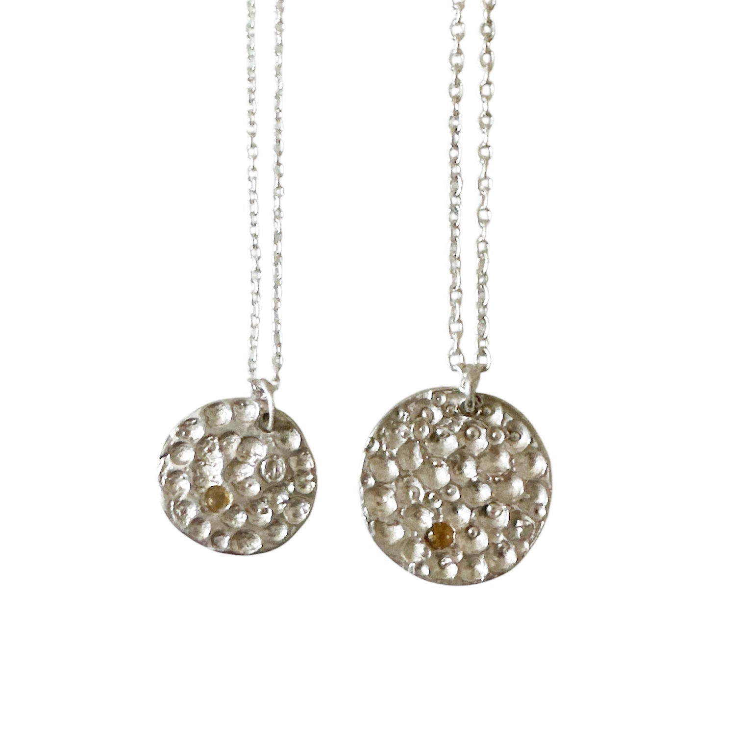 The Spot of Light necklace by FR | Art Jewellery features a sterling silver chain with a round pendant set with clear stones and a single citrine, showcased on a white background.