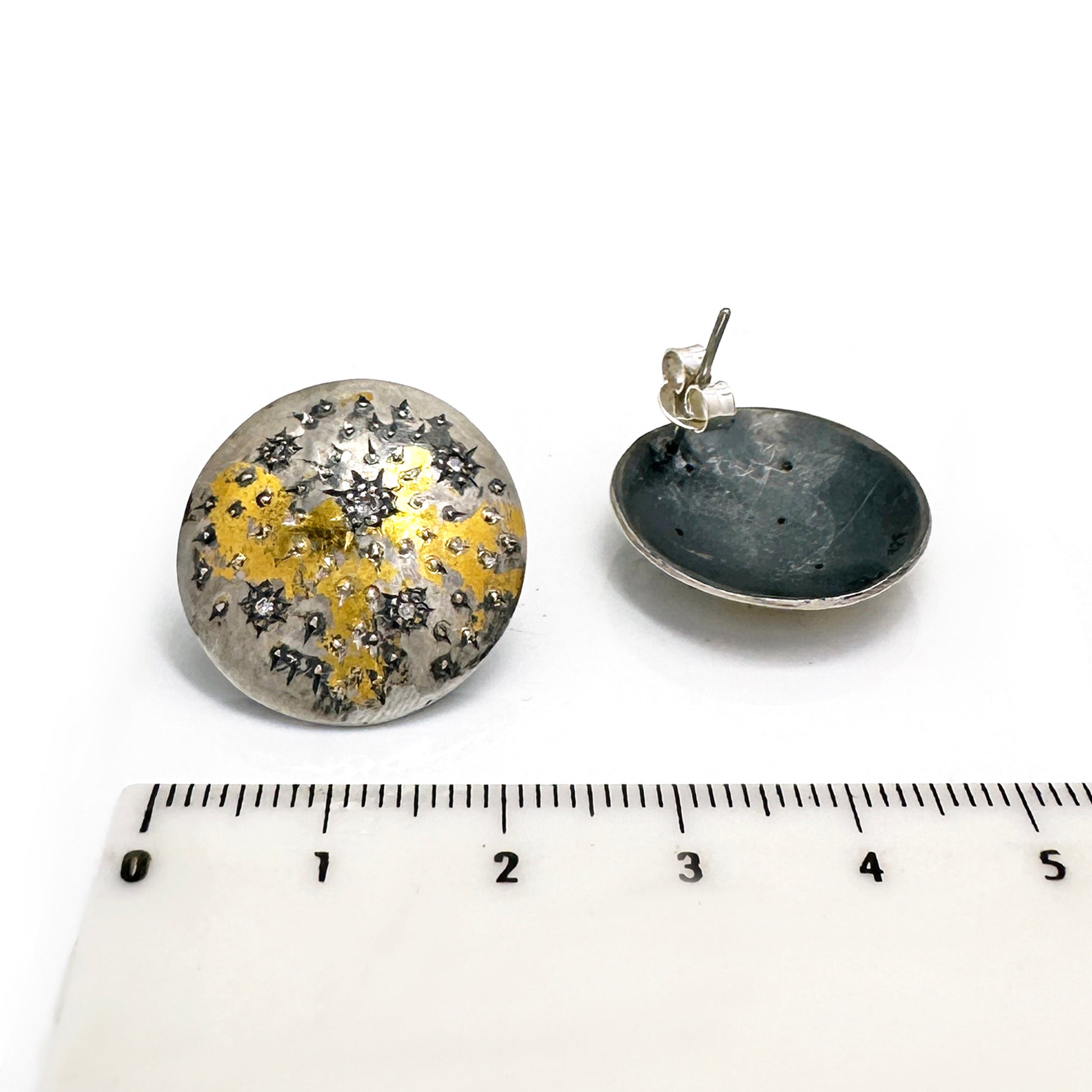 The Starburst Earrings by FR | Art Jewellery are a stunning pair of round metallic earrings with a textured surface, showcasing speckled patterns of gold and black on a silver base. This gold-plated, handmade jewellery design evokes the beauty of a starry night or cosmic theme, making it perfect for custom-made orders.