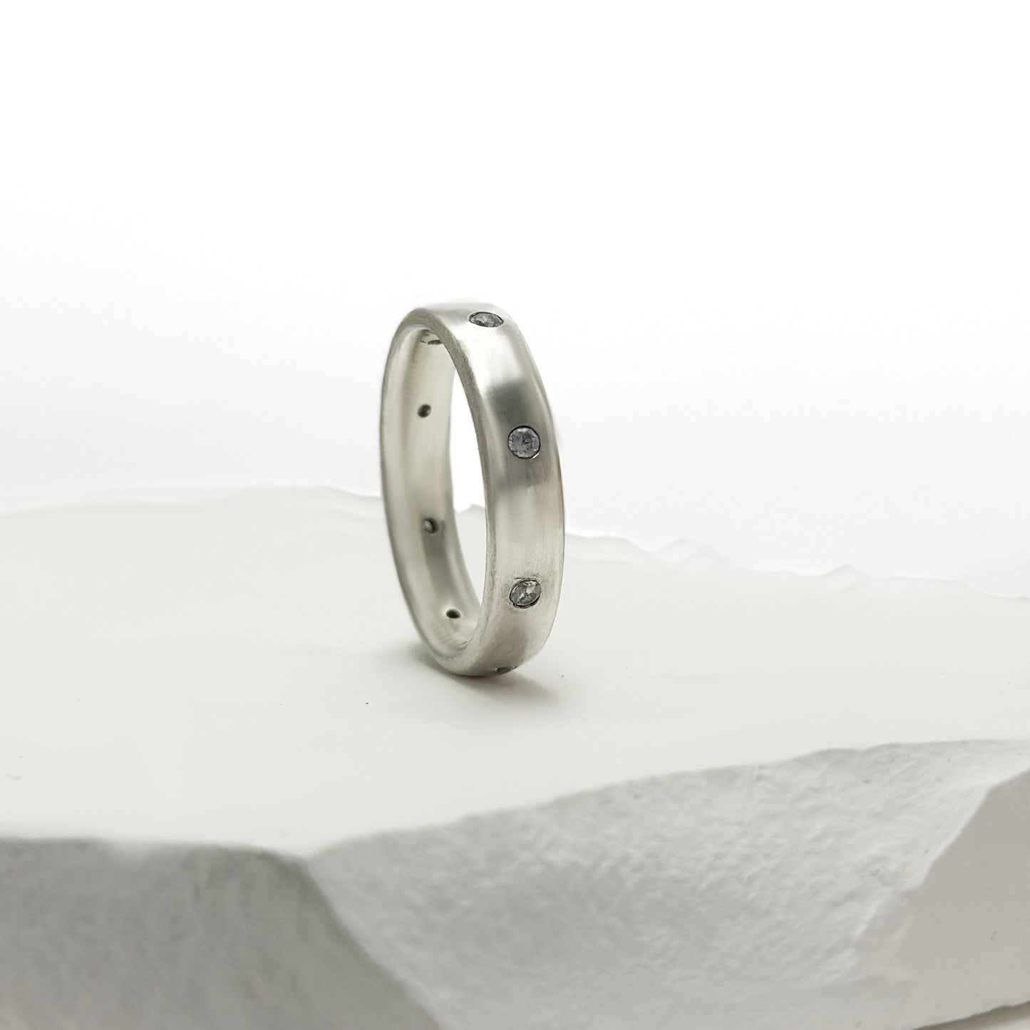 The FR | Art Jewellery Sterling Silver Diamond Band Ring features multiple small white diamonds evenly spaced around the sleek silver band, shown on a white background.