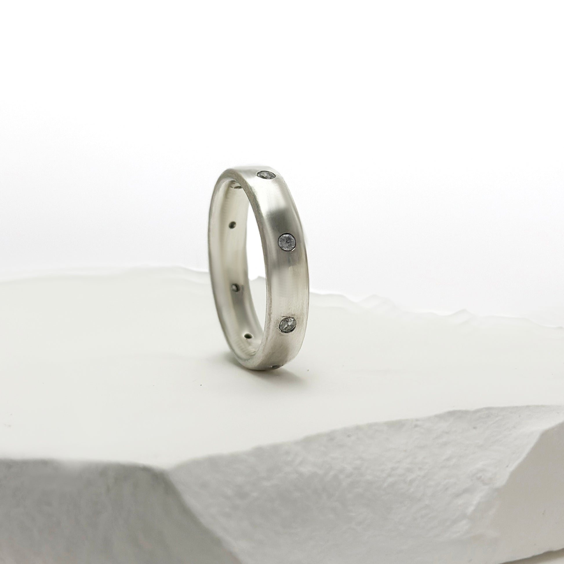 The FR | Art Jewellery Sterling Silver Diamond Band Ring features multiple small white diamonds evenly spaced around the sleek silver band, shown on a white background.