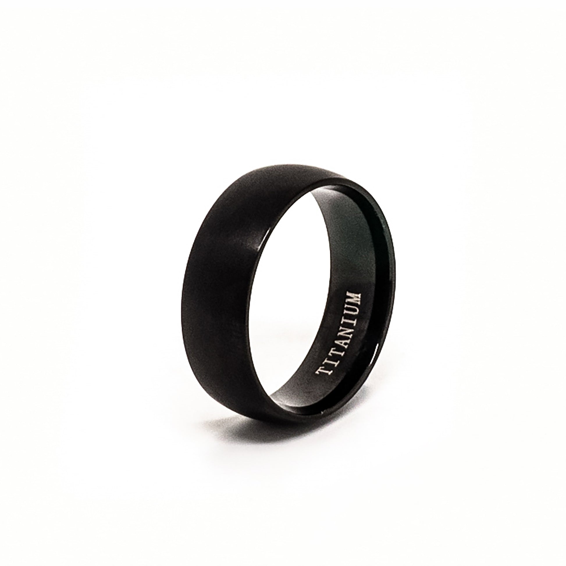 The Titanium Black Ring by FR | Art Jewellery is a comfort-fit titanium band with a black matte finish, shown upright on a white background and engraved with "TITANIUM" inside.