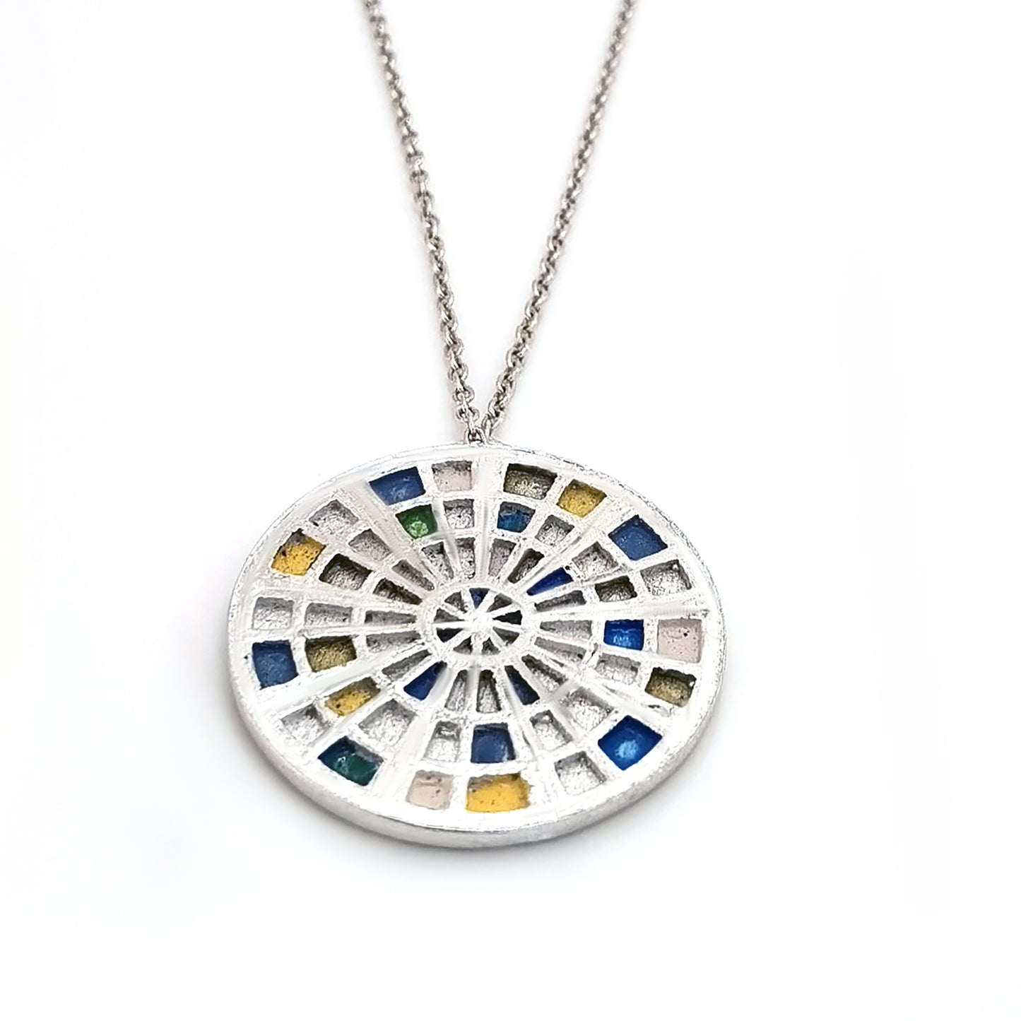 Introducing the "Talis Necklace blue 70cms" by FR | Art Jewellery—an elegant silver piece adorned with a round pendant that features an intricate stained glass window design. This mosaic pattern is comprised of small blue, green, yellow, and white squares arranged in a captivating circular layout. For the perfect ensemble, pair it with our gold-plated earrings or explore our custom-made options for unique handmade jewellery pieces.