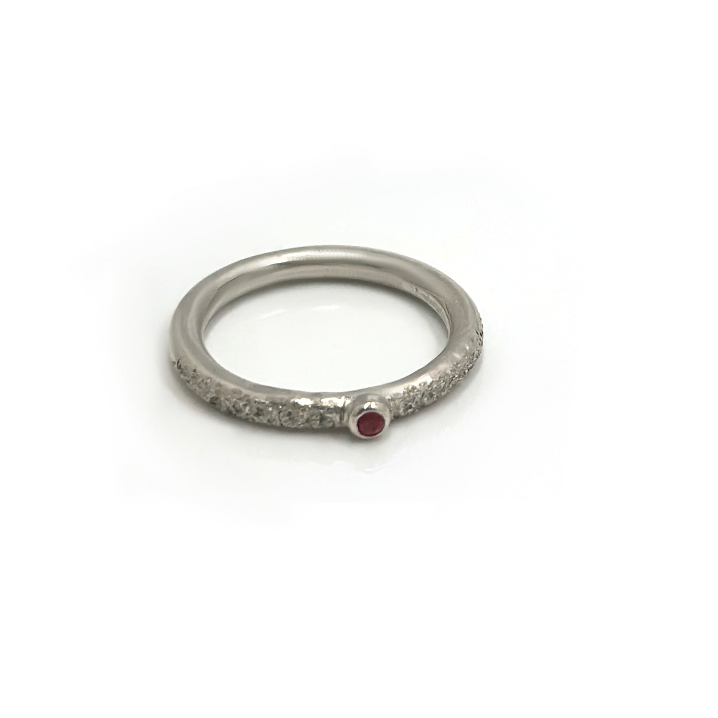 The FR | Art Jewellery Tinytoo Sterling Silver Ring with Ruby Gemstone features a textured band and a small round ruby, elegantly displayed on a white background.