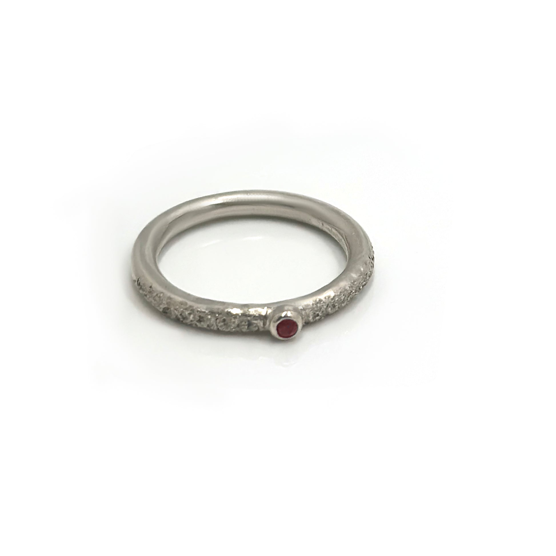 The FR | Art Jewellery Tinytoo Sterling Silver Ring with Ruby Gemstone features a textured band and a small round ruby, elegantly displayed on a white background.
