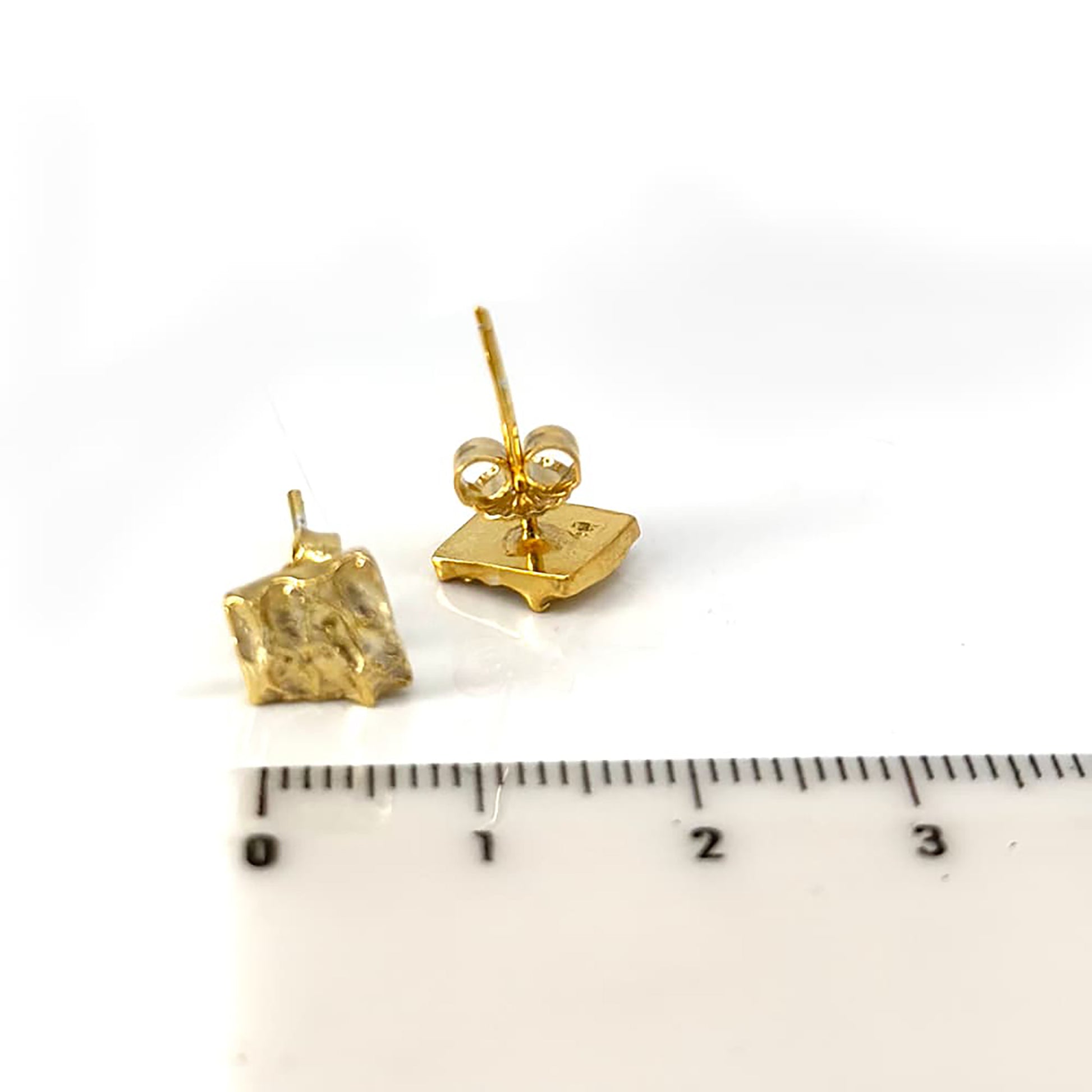 The Tribu Earrings by FR | Art Jewellery are displayed against a white background. These small, square-shaped gold-plated earrings feature a textured, wavy surface and come with standard post and butterfly backings, exemplifying exquisite handmade jewellery.