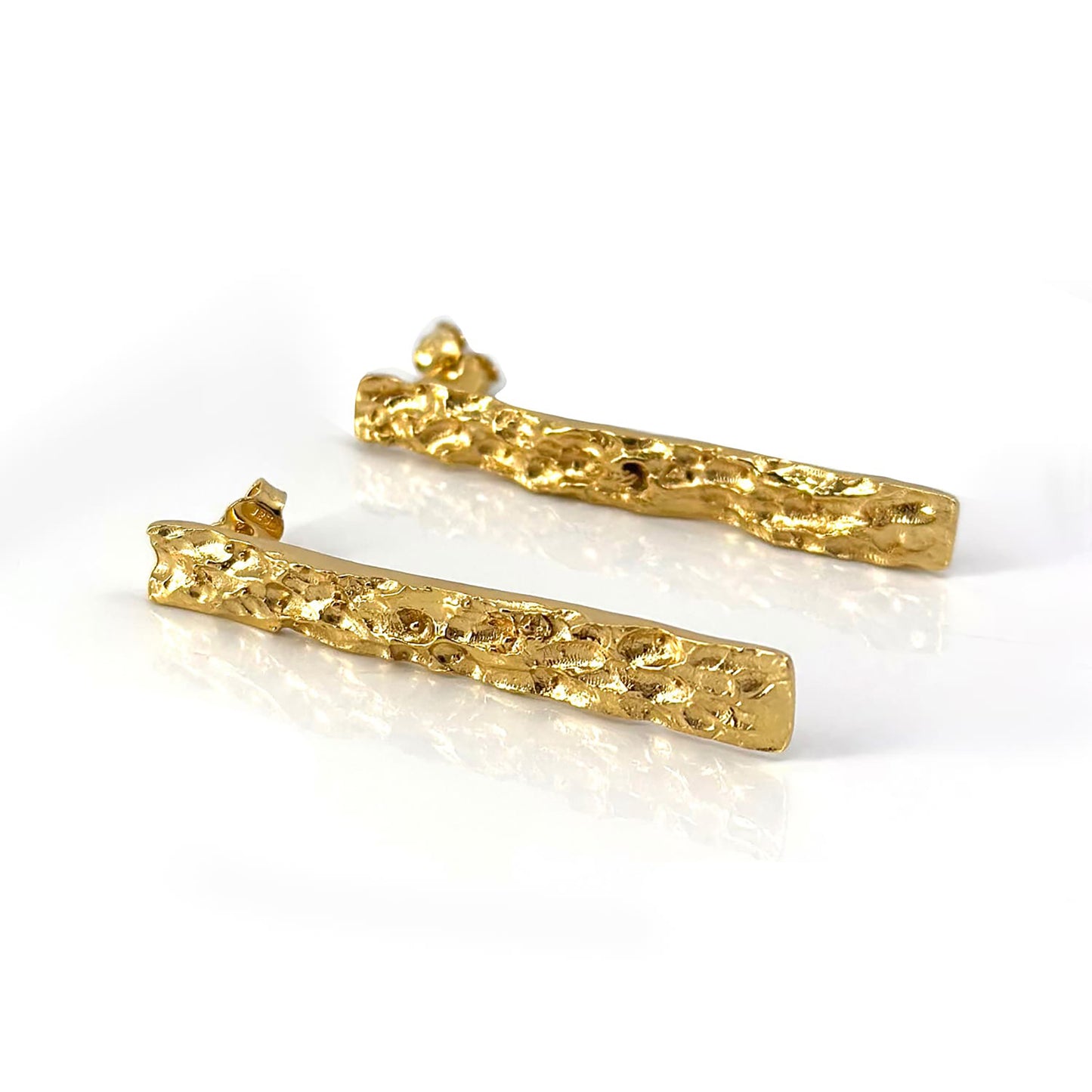 The Tribu Long Earrings by FR | Art Jewellery are a set of exquisitely crafted, gold-plated earrings featuring long, textured and jagged irregular surfaces. These handmade pieces boast a three-dimensional, organic design that resembles molten metal and are elegantly displayed against a clean, white background.