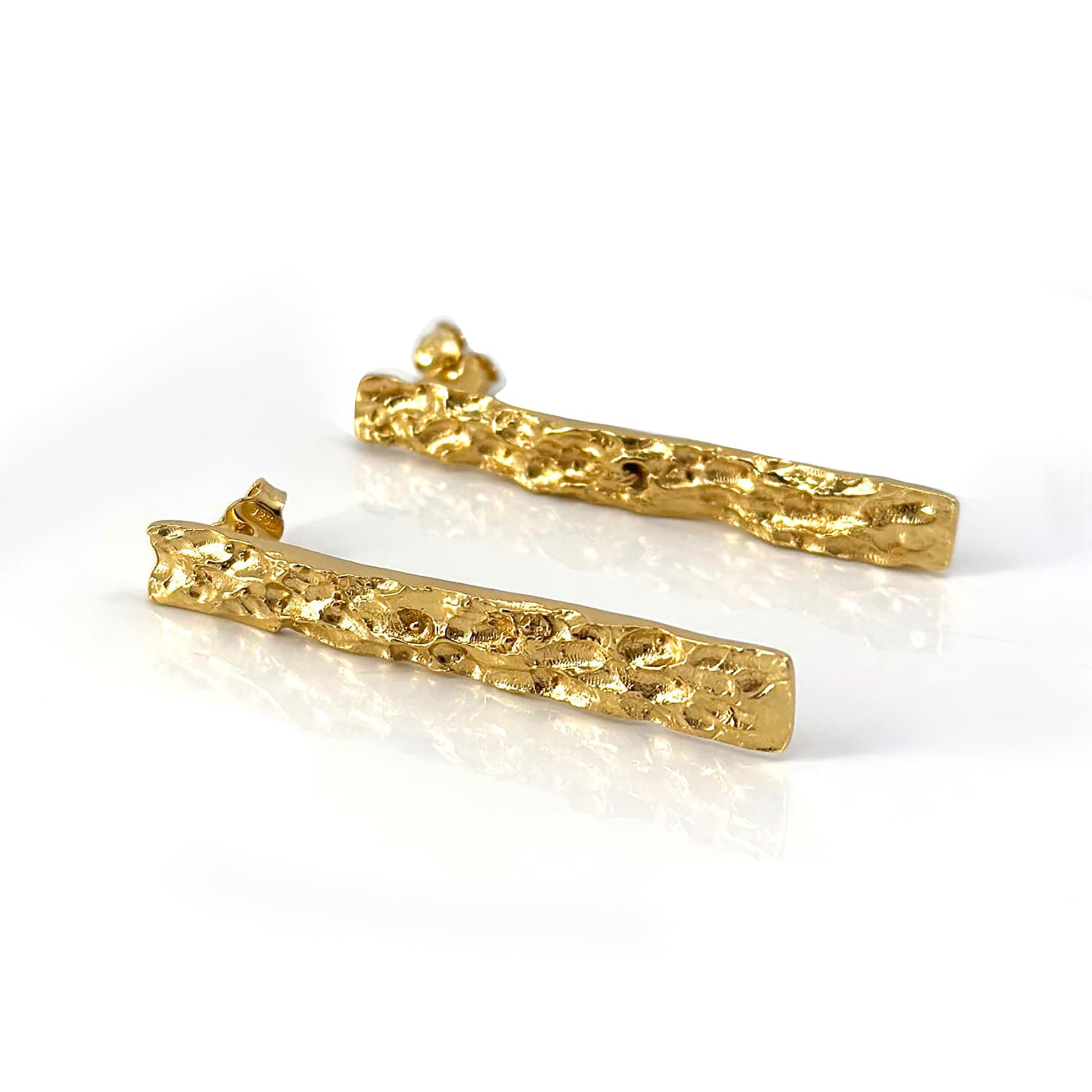 The Tribu Long Earrings by FR | Art Jewellery are a set of exquisitely crafted, gold-plated earrings featuring long, textured and jagged irregular surfaces. These handmade pieces boast a three-dimensional, organic design that resembles molten metal and are elegantly displayed against a clean, white background.