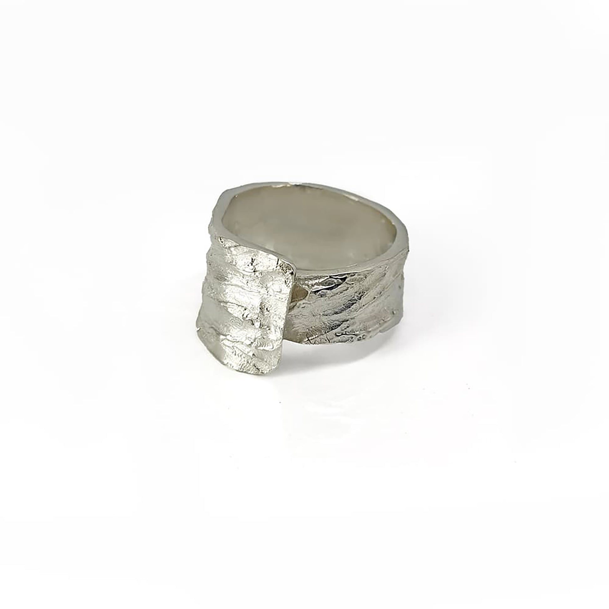 The Tribu Ring from FR | Art Jewellery is showcased against a pristine white background. This handmade piece of jewellery boasts a textured gold finish and a wide band, featuring an innovative design with part of the band overlapping to create a layered effect on one side. Custom orders are available to match gold-plated earrings for a cohesive set.