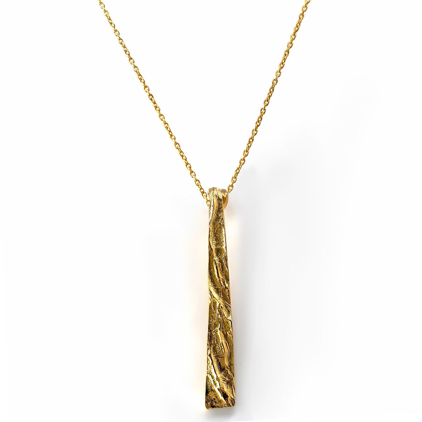 Introducing the Tribu Necklace by FR | Art Jewellery, a gold necklace featuring a long, textured, vertical bar pendant. The pendant boasts an organic, uneven surface and gracefully hangs from a delicate gold chain. This piece of handmade jewellery is minimalist yet striking, offering a touch of artisanal elegance that you can personalize with custom-made orders.