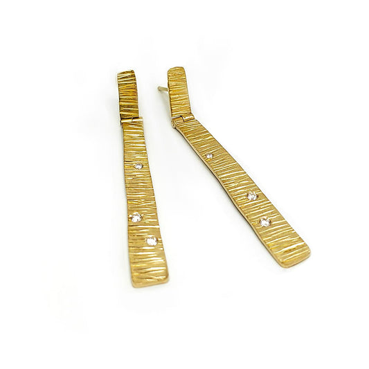 Introducing the Tribu Gold Diamonds Earrings by FR | Art Jewellery, a stunning pair of long, rectangular earrings with a luxurious gold-plated finish and a textured surface. Adorned with small, sparkling rhinestone accents, these handmade pieces are beautifully displayed on a plain white background and are an excellent choice for custom-made orders.