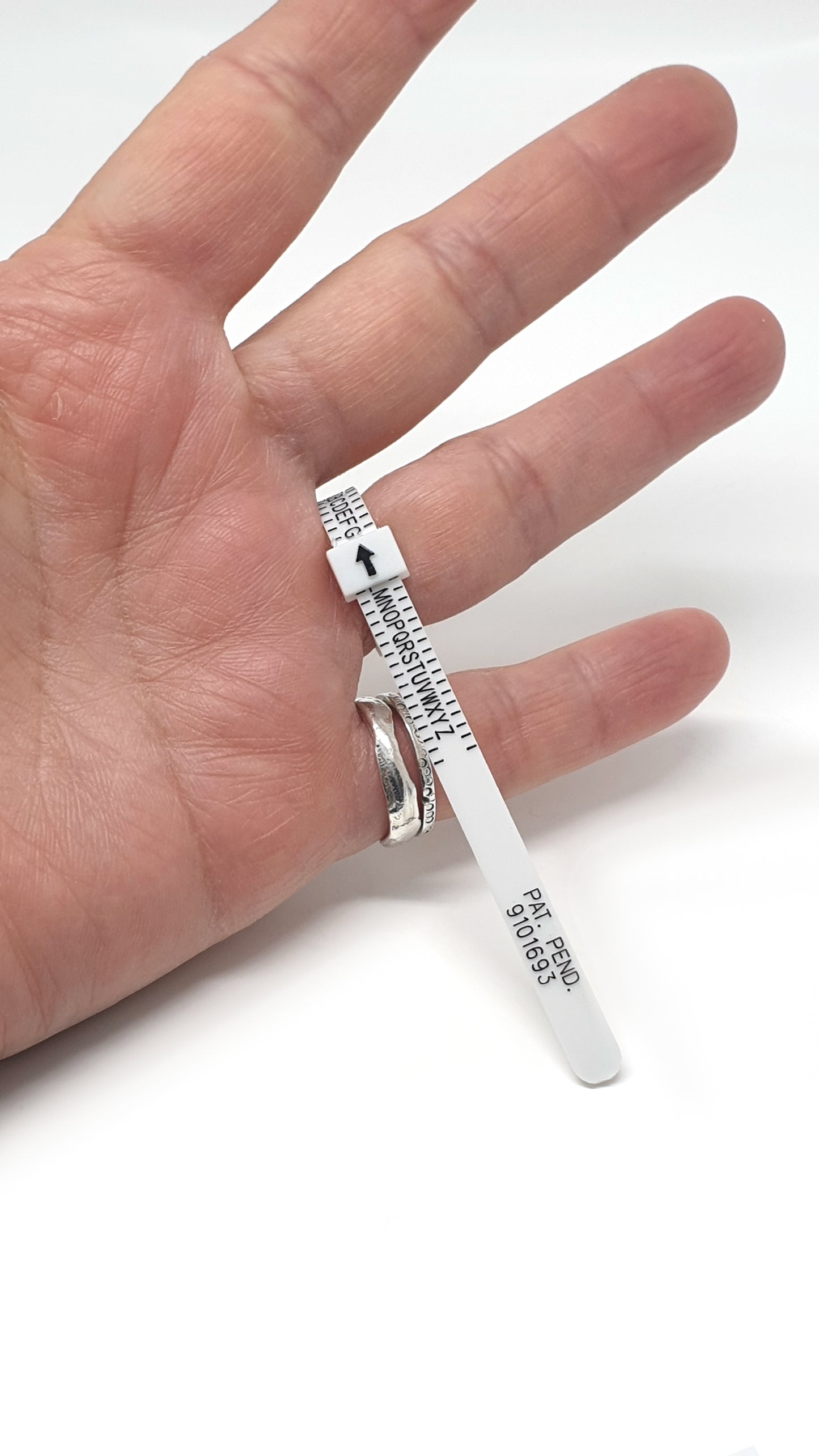 The FR | Art Jewellery Ring Sizer is a white plastic tool resembling a zip tie, labeled with letters A through Y and an upward-pointing black arrow on one end. Along its length, it features "SIZE," "PAT. PEND," and "9101933" for accurate ring size measurement.