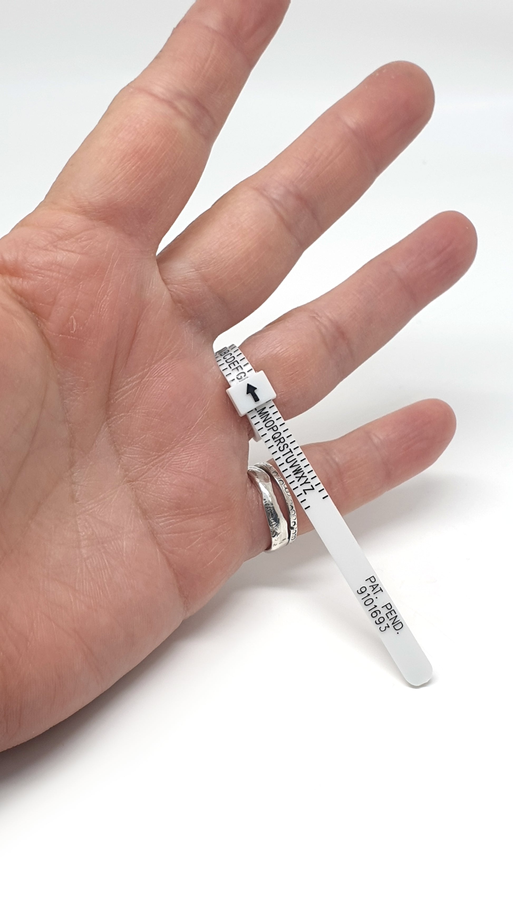 The FR | Art Jewellery Ring Sizer is a white plastic tool resembling a zip tie, labeled with letters A through Y and an upward-pointing black arrow on one end. Along its length, it features "SIZE," "PAT. PEND," and "9101933" for accurate ring size measurement.