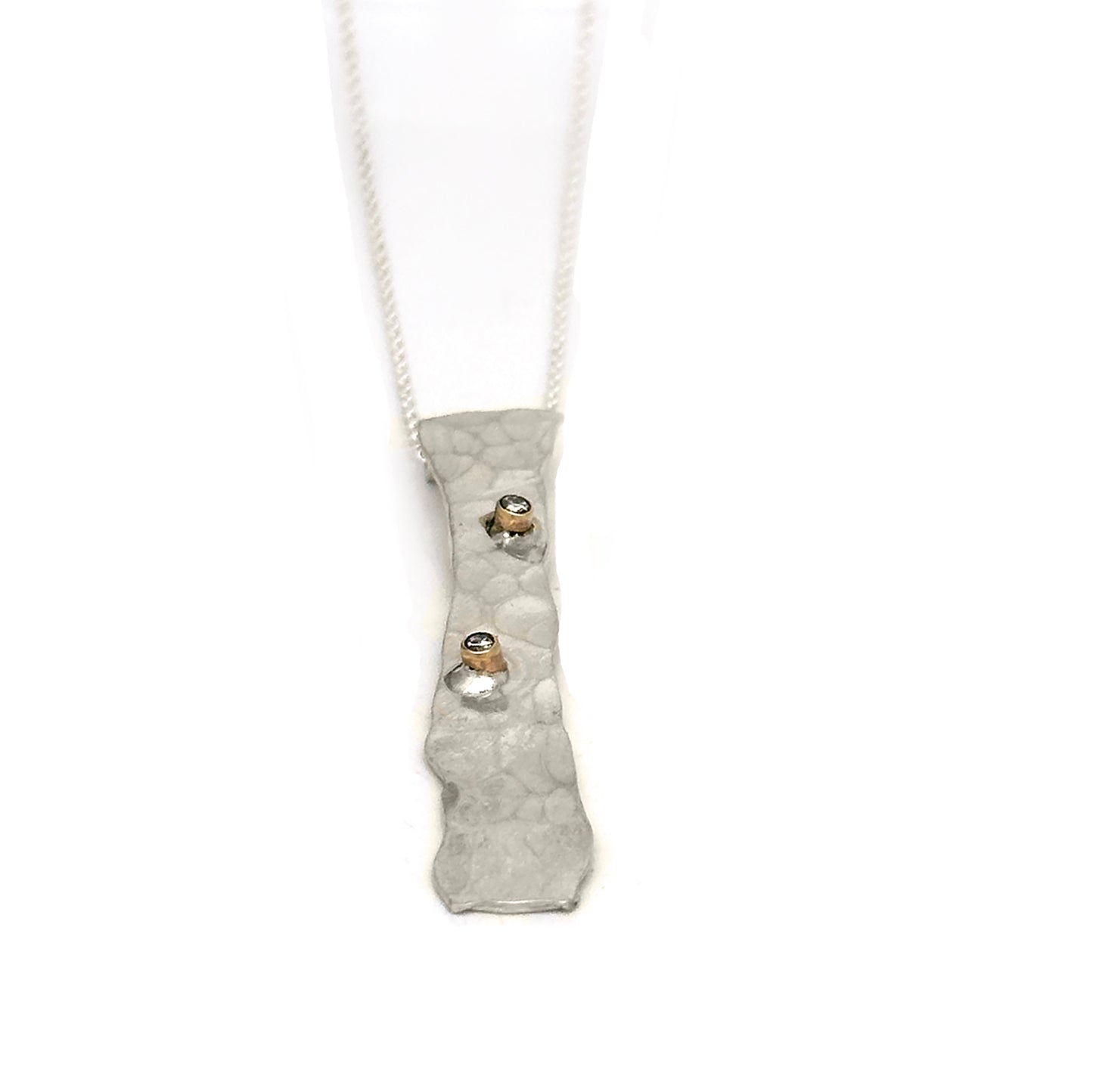 The "Shooting Star Necklace" by FR | Art Jewellery features a silver, rectangular pendant with a hammered texture and two small, sparkling gemstones. This pendant is suspended on a fine silver chain and showcases an uneven, organic shape that adds an artisanal touch to this handmade jewellery design. The background is plain white.