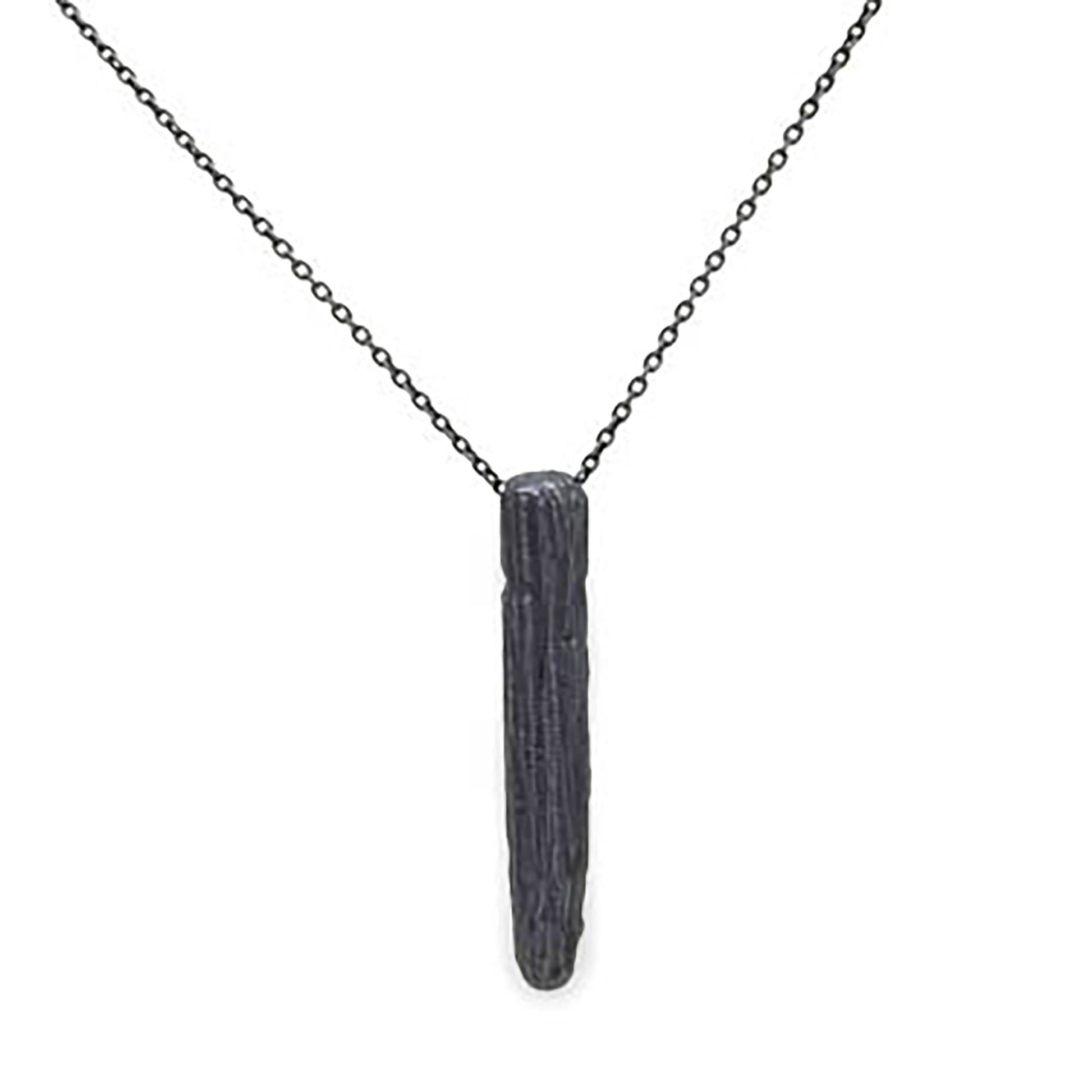 The Succulent Garden Necklace Oxidized by FR | Art Jewellery showcases a minimalist design with a thin, elongated, textured black pendant hanging from an elegant black chain. The pendant's rough, natural texture imparts an organic touch to the overall aesthetic. Pair it with our gold-plated earrings for a complete look.